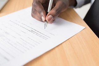 Picture of a person signing a document with a pen.